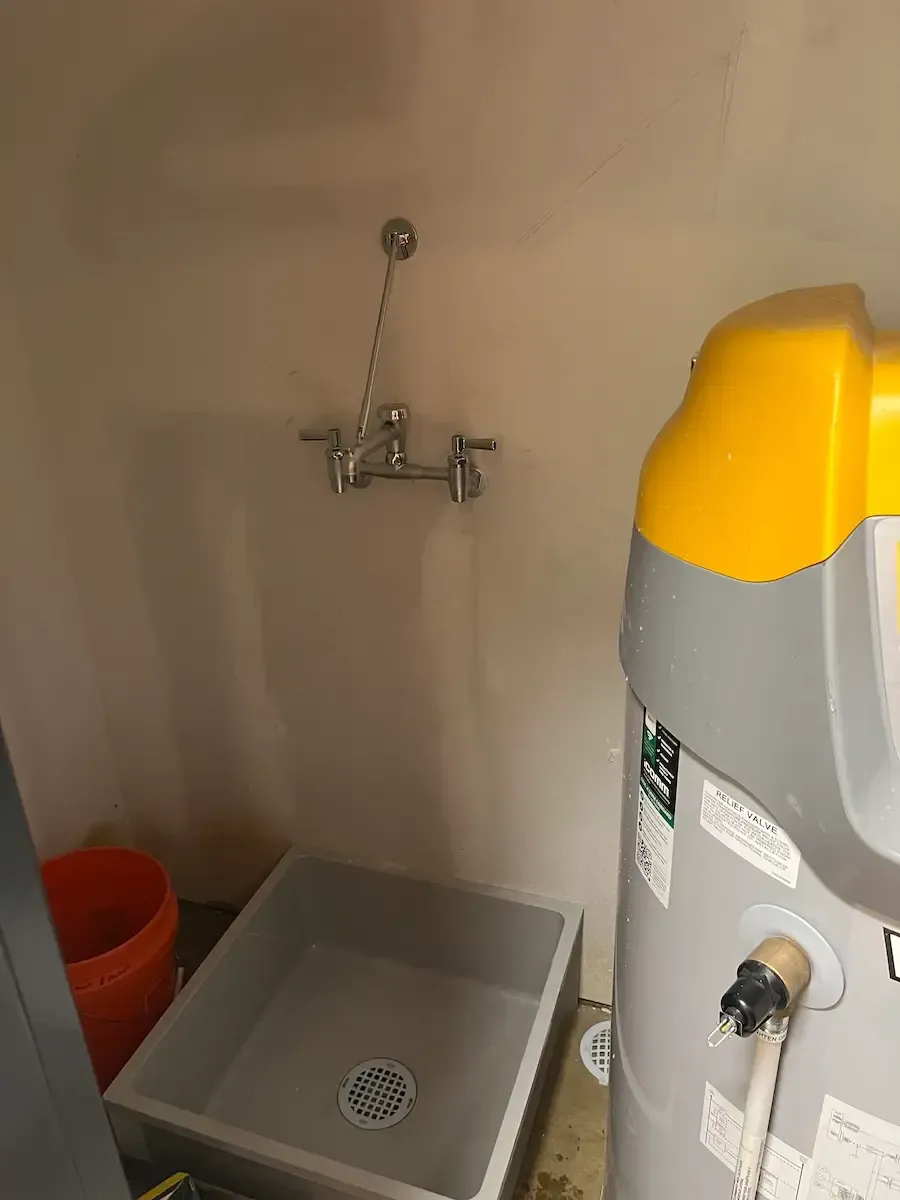 Sink and faucet in utility room, next to a water heater and bucket.