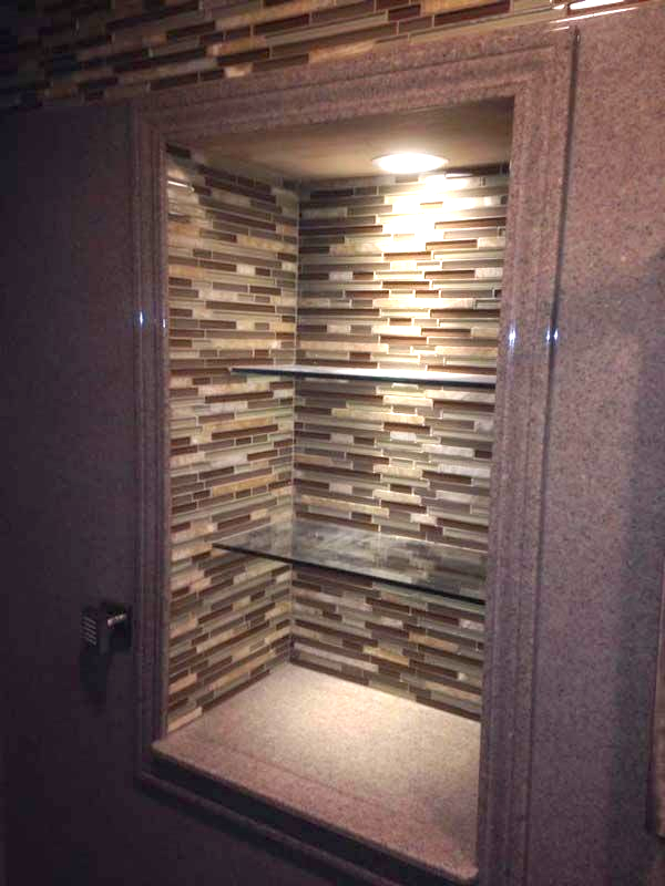Recessed shower shelf with mosaic tile, glass shelves, and overhead lighting.