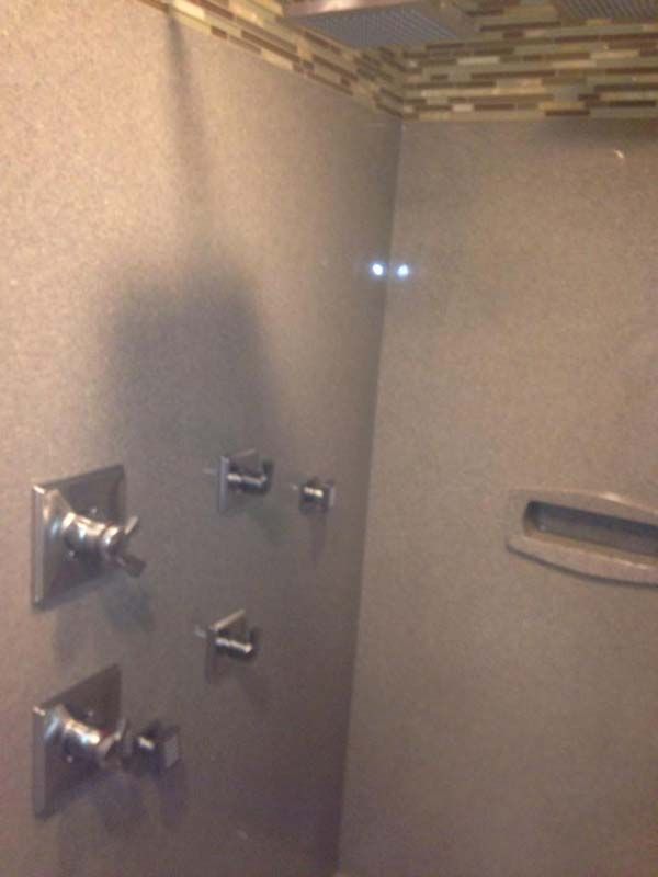 Shower interior with multiple chrome fixtures against gray tile. Upper border has mosaic tile.