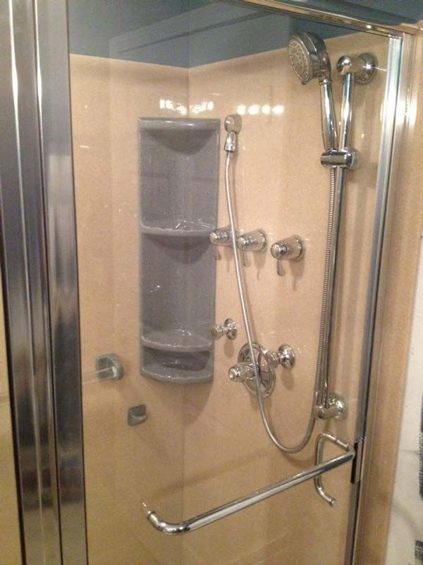 Shower stall with chrome fixtures, built-in shelving, and beige tile walls.