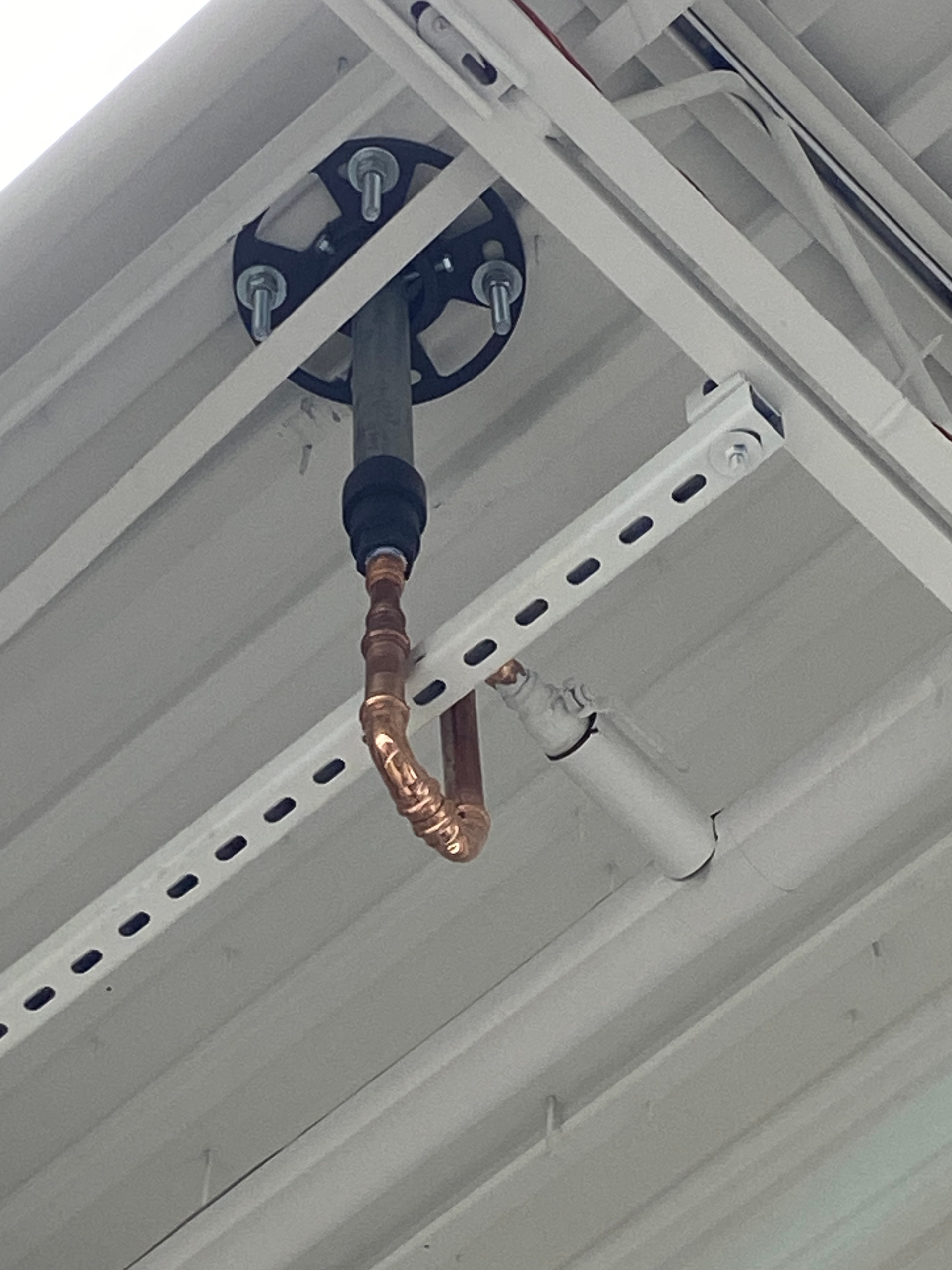 Copper pipe and wiring hanging from a white metal building structure.