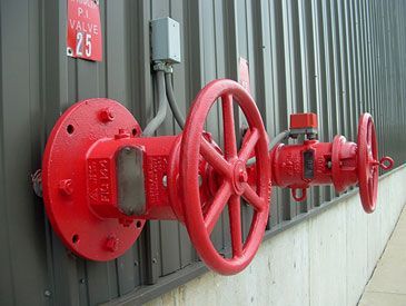 Red fire hydrant valve mounted on a building's exterior wall.