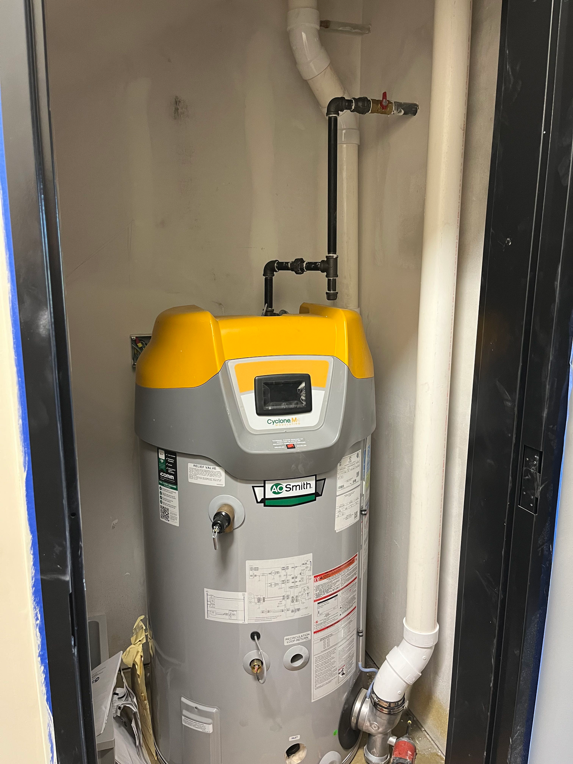 Water heater in a small, enclosed space, with connected pipes and valves.