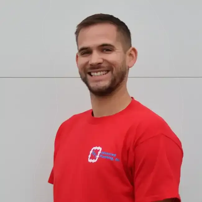 Man smiling, wearing a red t-shirt with a logo, standing in front of a white wall.