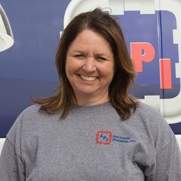 A smiling person in a gray sweatshirt with the Advanced Plumbing, Inc. logo, posed in front of a blue company vehicle.