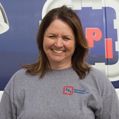 A smiling person in a gray sweatshirt with the Advanced Plumbing, Inc. logo, posed in front of a blue company vehicle.