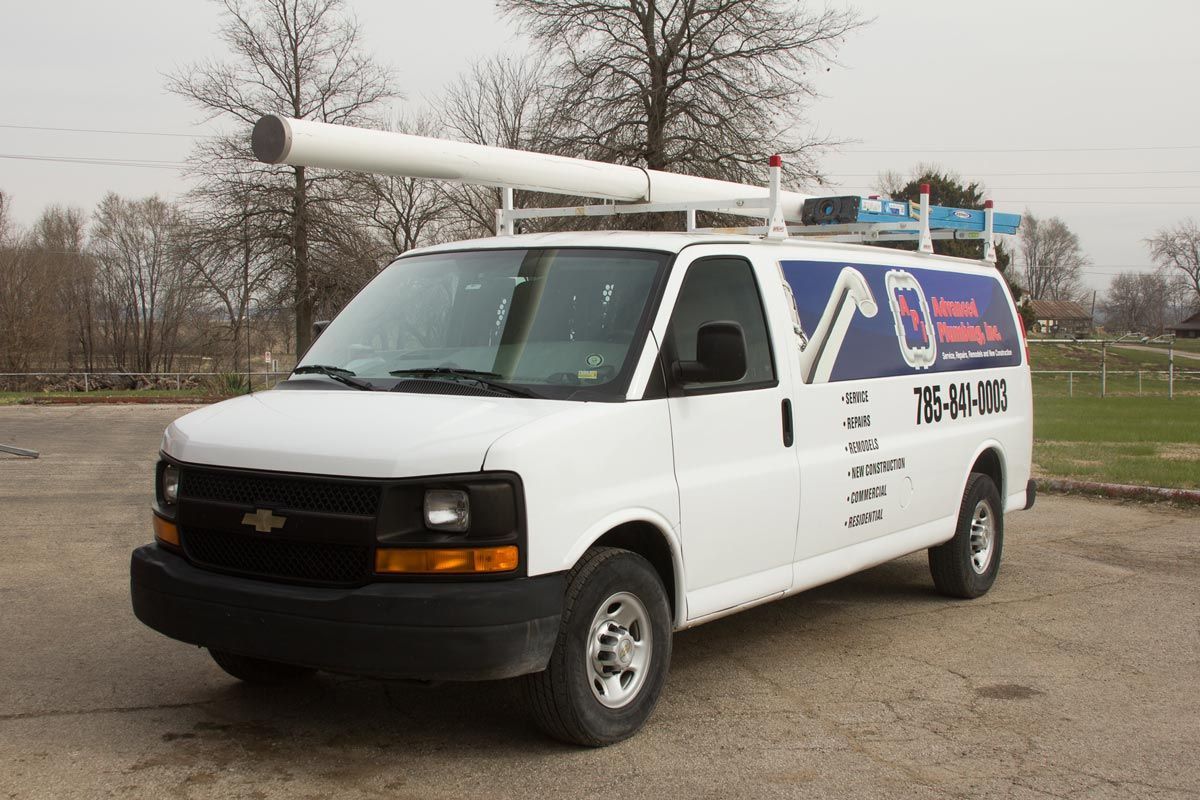 White Chevrolet work van with logo and telephone number parked outside. Roof rack with large white tube.