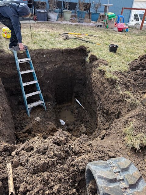 Person on ladder in large excavation, likely for underground utility work. Outdoor setting.