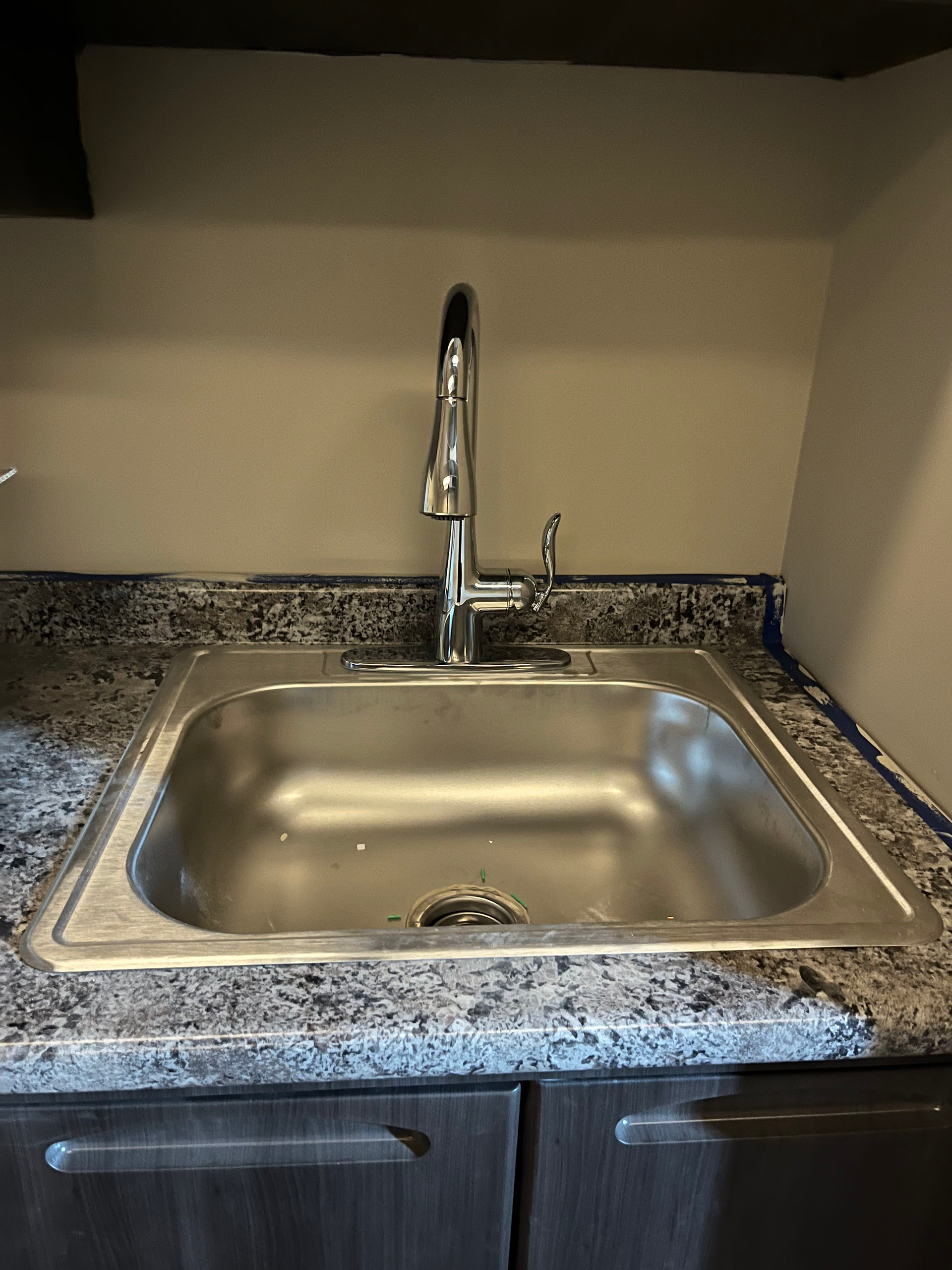 Stainless steel kitchen sink with chrome faucet, on a speckled countertop.