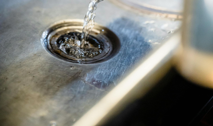 Water pouring from a faucet into a stainless steel kitchen sink drain.