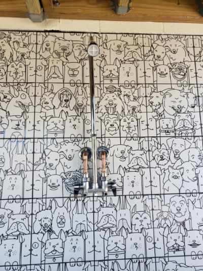 Wall mural of numerous line-art dog faces. Two taps are mounted in front. Grid lines overlay the artwork.