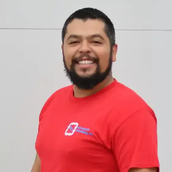 Man in red t-shirt smiles, a full beard. The shirt has a logo, set against a plain background.
