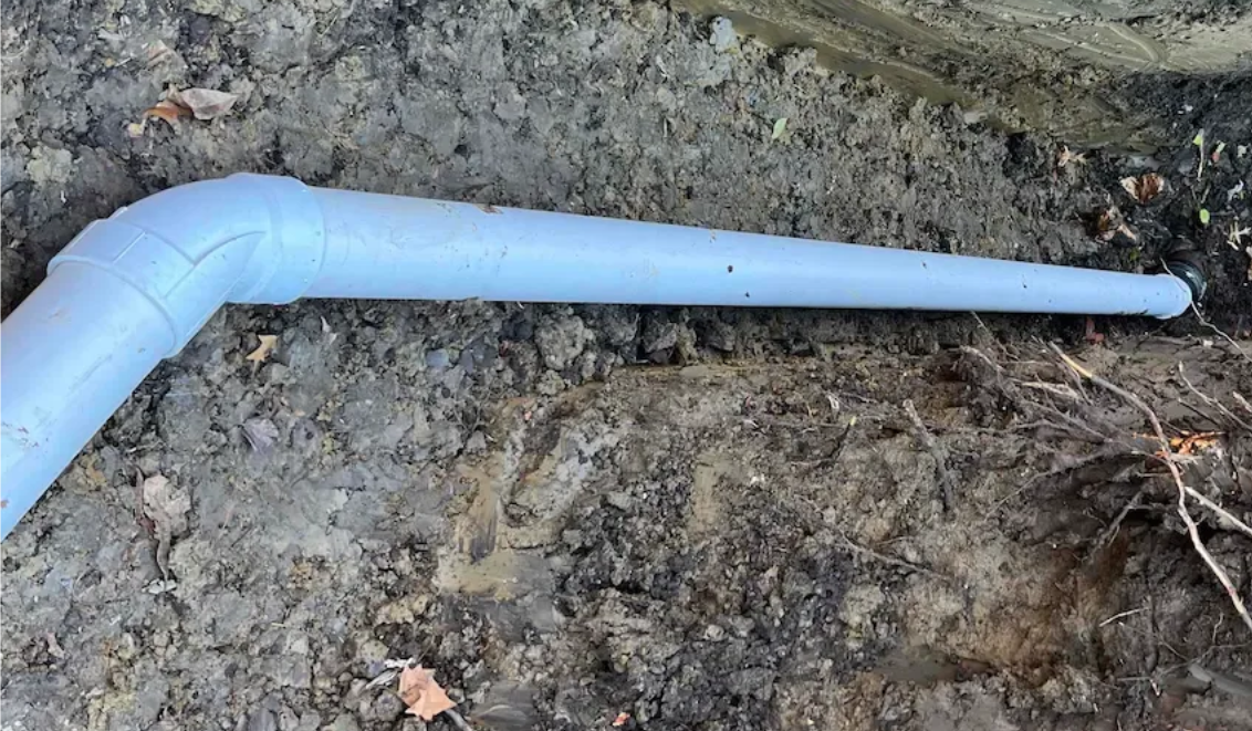 White PVC pipe in dirt, bent at an angle.