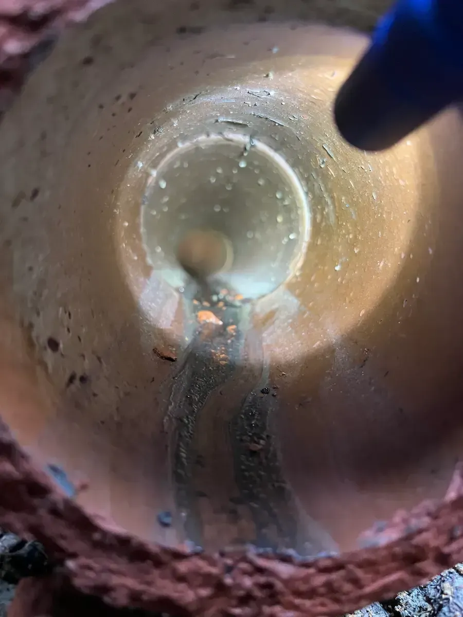 Inside view of a pipe: Brown interior with water flowing down. A gloved hand is visible.