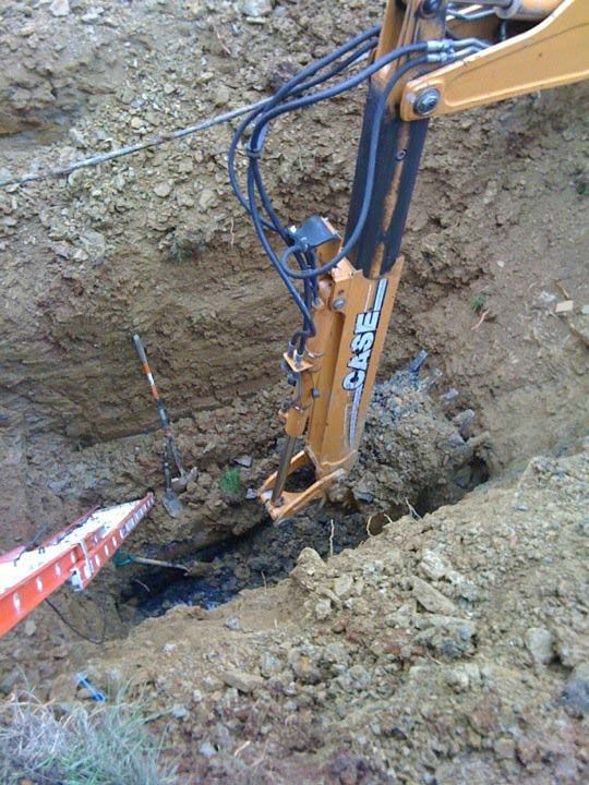 A Case backhoe excavating in a dirt pit, with an orange ladder.