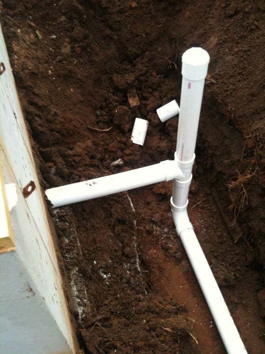 PVC pipes in a trench, forming a drainage system, with exposed soil and a white cap.