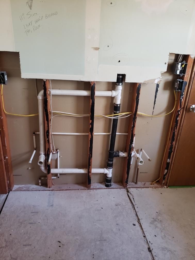 Piping and electrical work exposed in a wall during a renovation. White and black pipes, yellow wires, and wood framing.