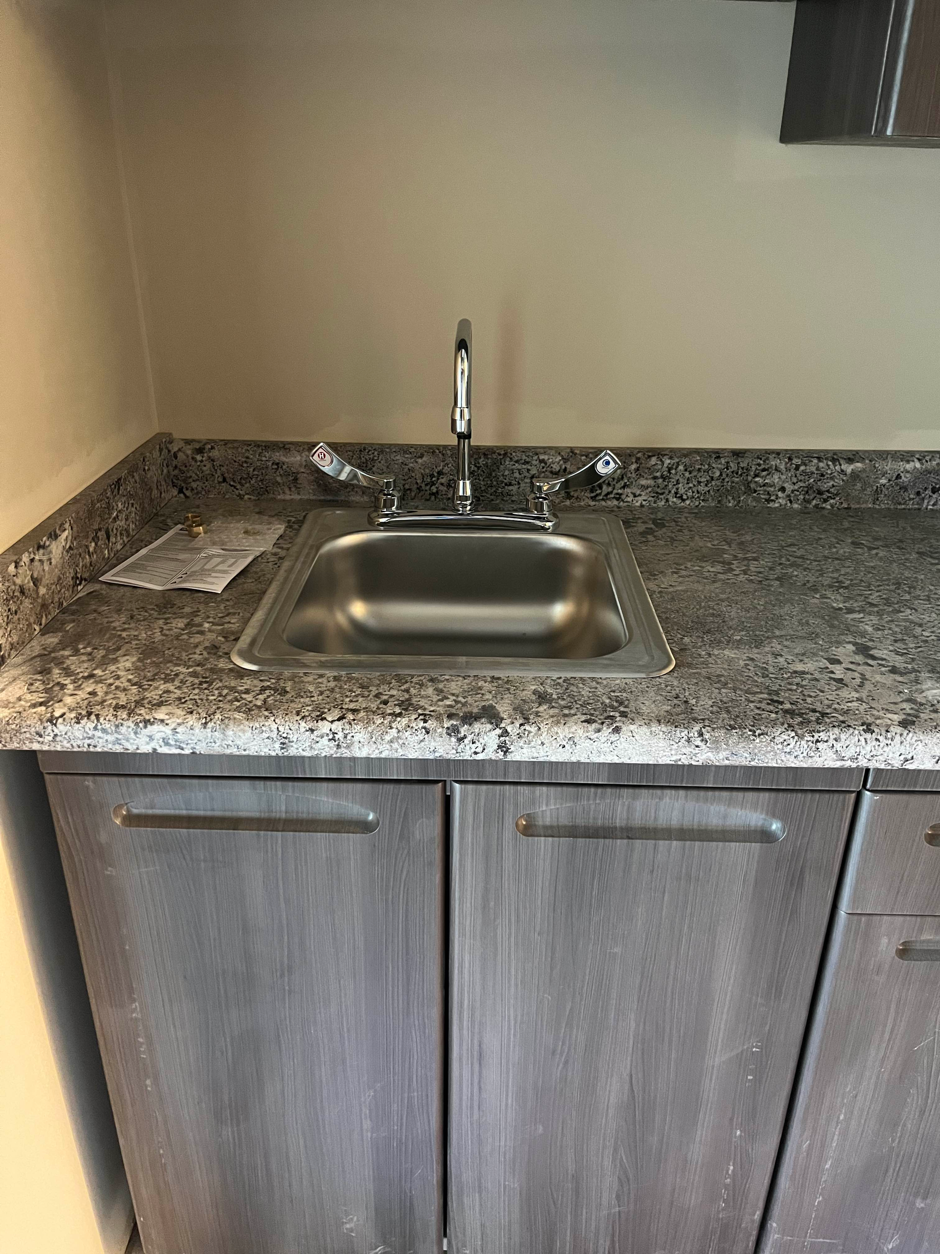 Stainless steel sink in a grey granite countertop above grey cabinets.