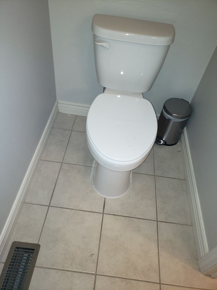 Toilet in a small bathroom with gray walls, white baseboards, and tile floor, a stainless steel trash can.