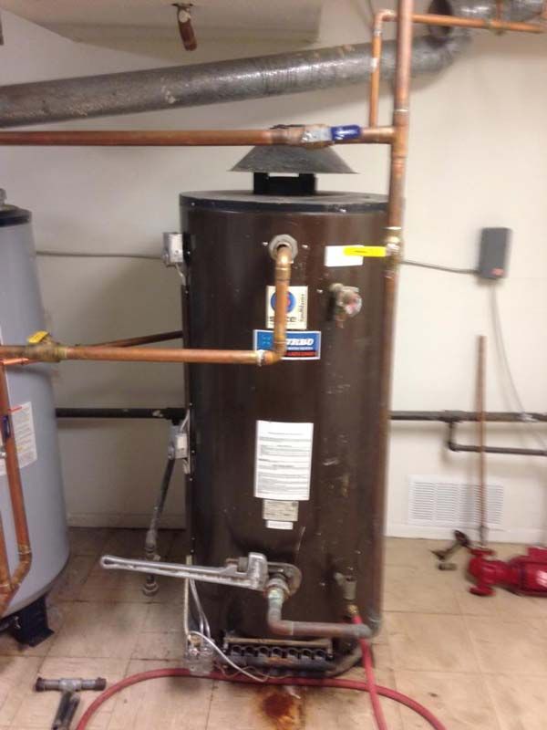 A brown water heater with copper pipes in a utility room.