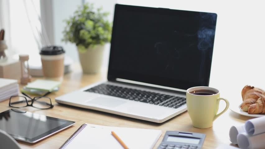 A laptop computer is sitting on a wooden desk next to a cup of coffee.