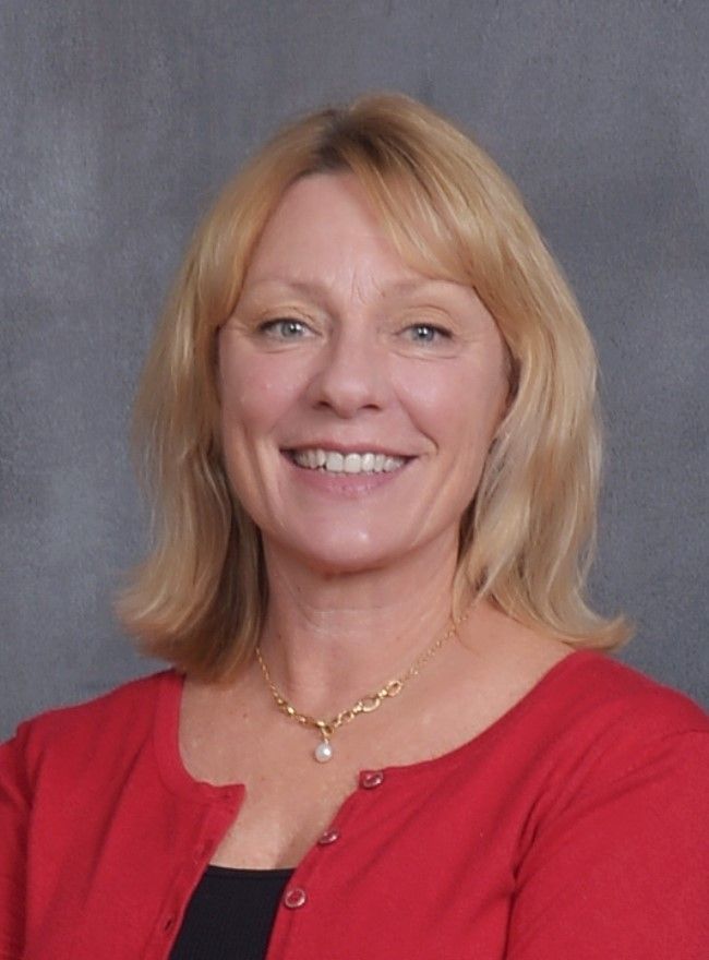 A woman wearing a red cardigan and a gold necklace is smiling for the camera.