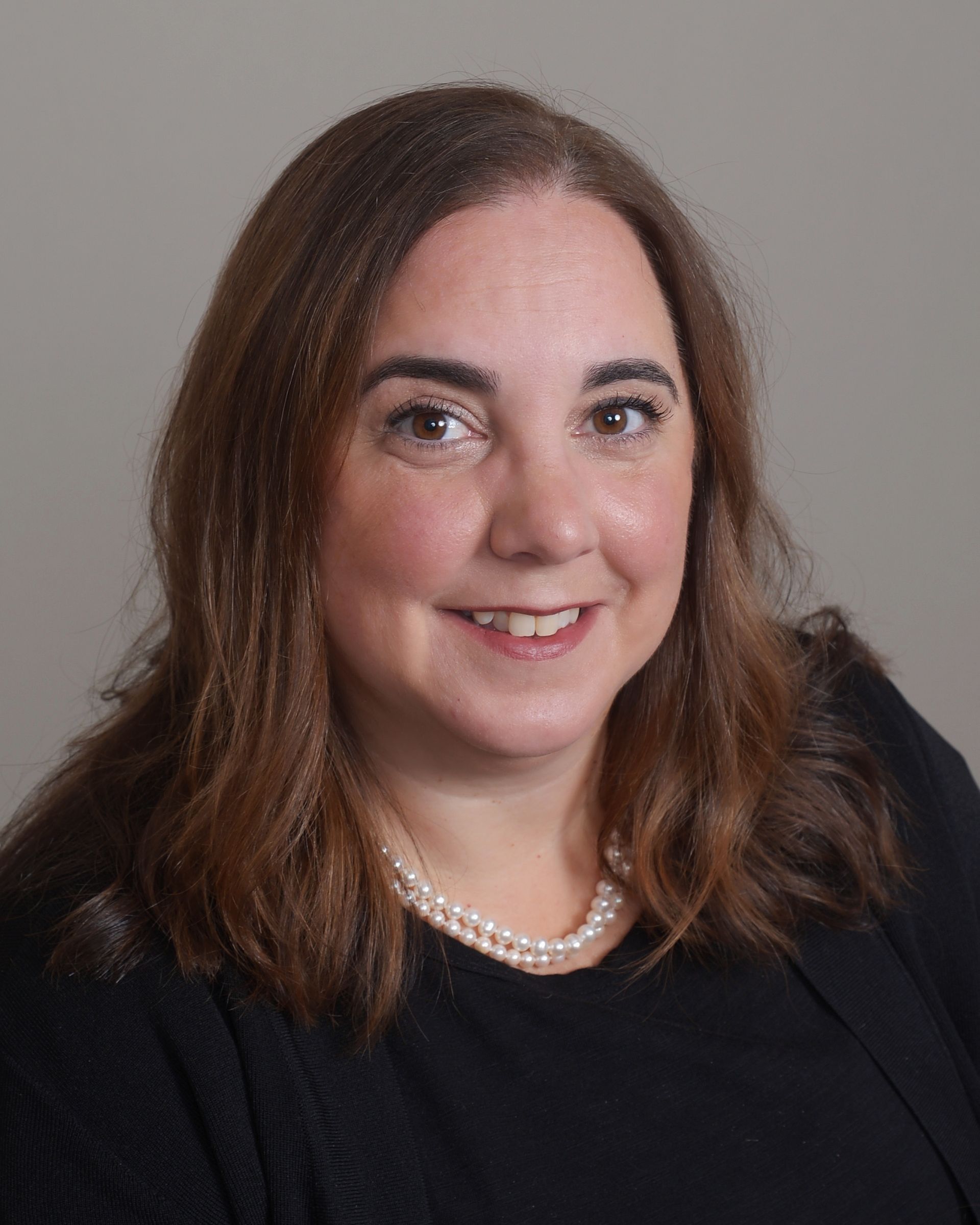 A woman wearing a black shirt and a pearl necklace is smiling for the camera.