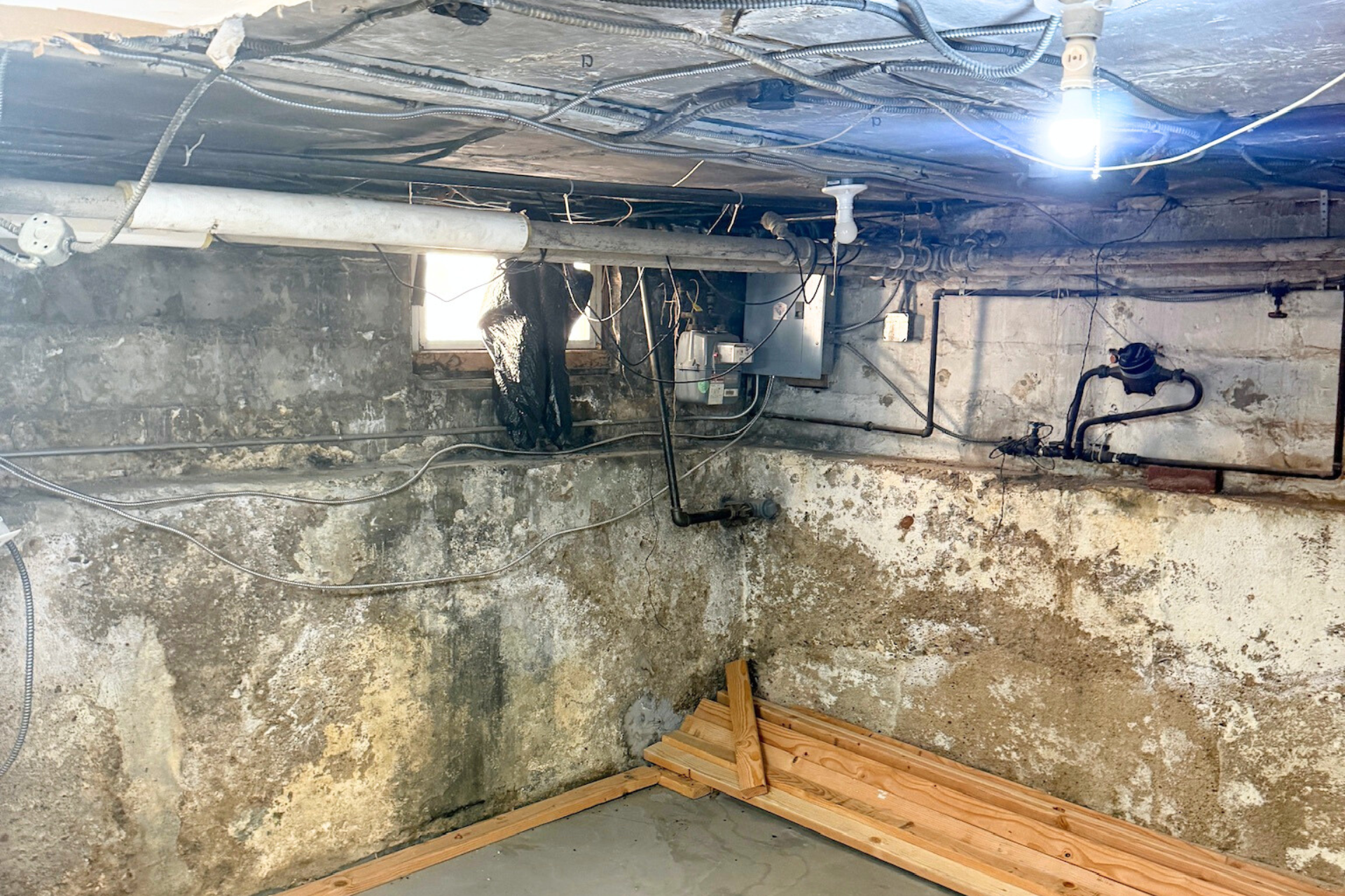 Basement before renovation — old concrete walls and exposed pipes in Brooklyn, NY.