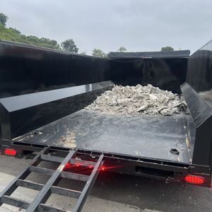 Black trailer with a ramp, loaded with rubble.