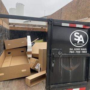 A black SA Junk Haul trailer loaded with cardboard boxes and other debris.