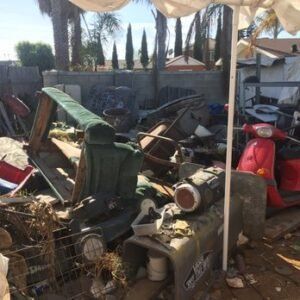 Pile of discarded items, including vehicle parts, under a white canopy in an outdoor area.