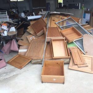 Pile of discarded wooden cabinet doors, drawers, and panels on a concrete surface.