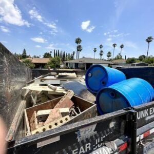 Dumpster filled with construction debris, including blue barrels, under a blue sky.