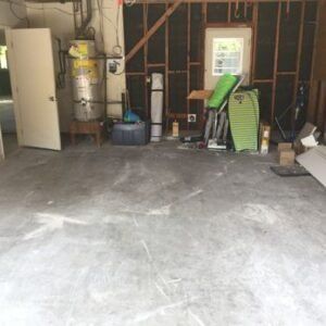 Garage interior, partially empty, with concrete floor. Storage items along the back wall, including a door and water heater.