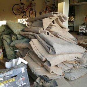 Pile of rolled-up carpet remnants in a garage; a miter saw and bikes are also visible.