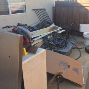 Pile of construction debris in a backyard, including wood, cardboard, wires, and a toilet.