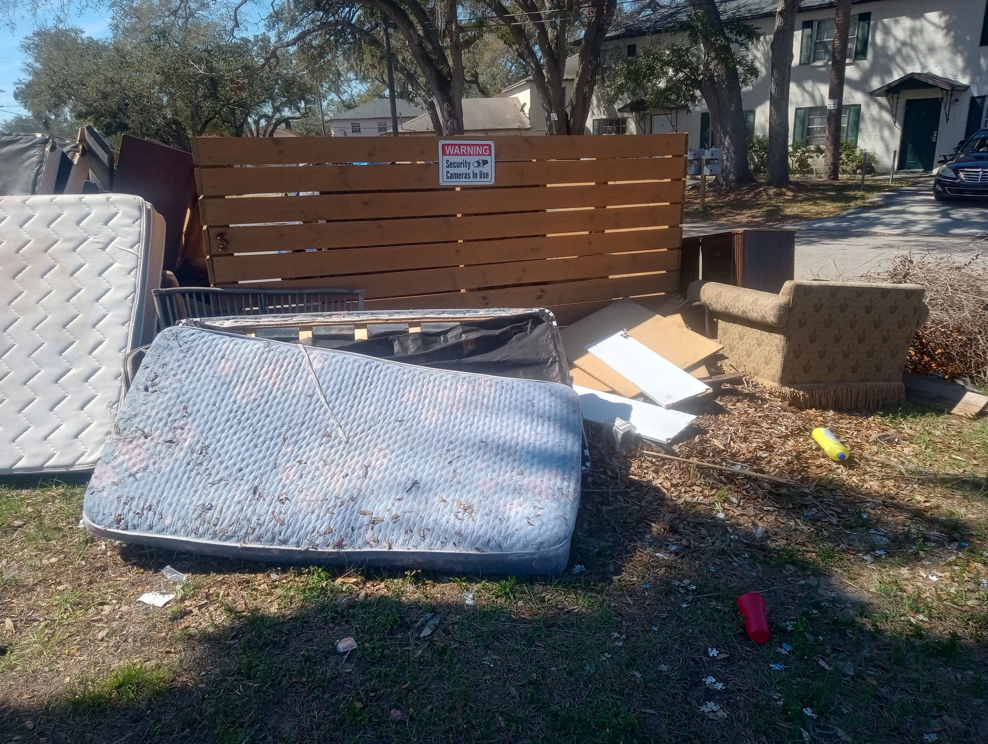 A mattress is sitting in the grass in front of a wooden fence.
