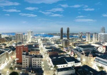 City skyline at night with lit buildings, streetlights, and a body of water in the distance.