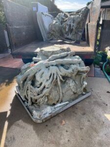 Dump truck bed filled with large, gray concrete sculptures; one is on the ground.