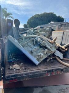 Dump truck bed filled with construction debris, including architectural elements, against a blue sky.