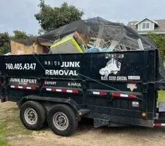 Black junk removal trailer filled with debris, phone number and company logo on the side.