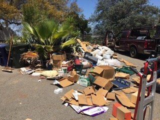 A pile of trash and cardboard boxes on a driveway next to a red truck and palm trees on a sunny day.