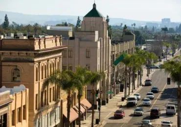 Street view of historic downtown buildings, palm trees, and traffic on a sunny day.
