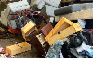 Pile of discarded furniture and debris including drawers, a bed frame, and sofa cushions.