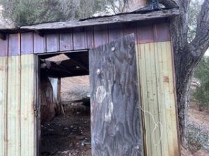 Dilapidated wooden shed with open door, weathered boards. Outdoors.
