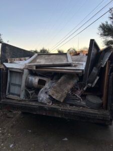 Truck bed filled with scrap metal and debris; gray sky background.