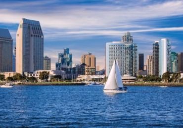 Sailboat on blue water with San Diego skyline.