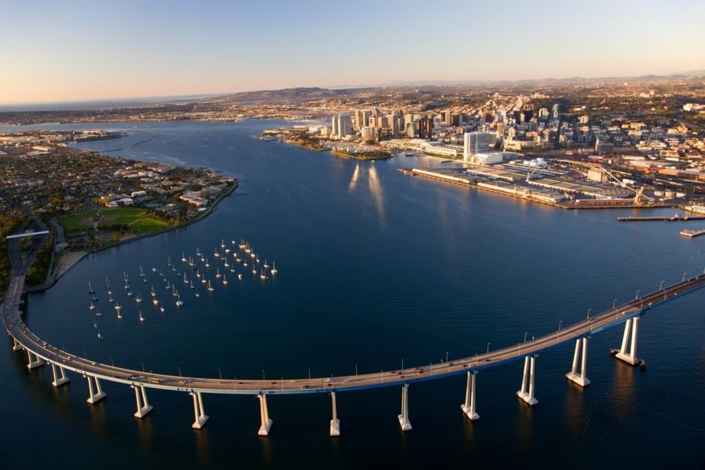 San Diego-Coronado Bridge spans blue water, connects city skyline and residential area, boats, sunlight.