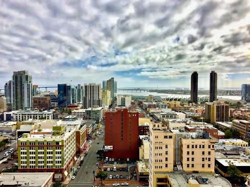 San Diego cityscape under a cloudy sky, with tall buildings, streets, and water in the distance.