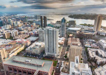 Aerial view of a city with tall buildings, a bridge over water, and a cloudy sky.